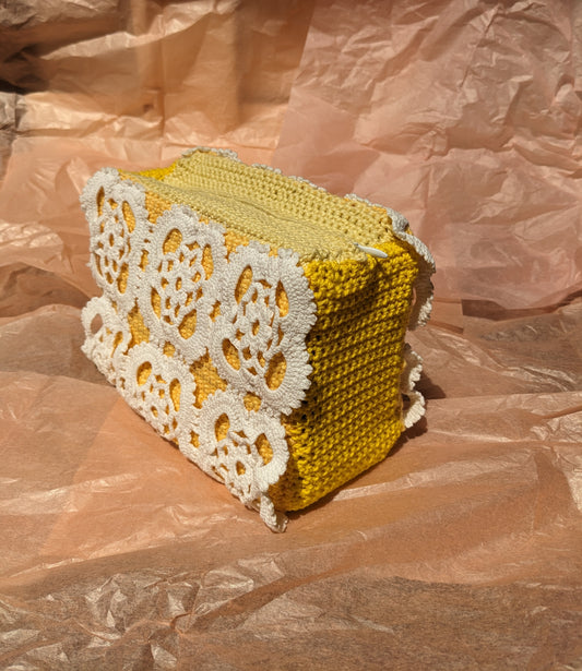Yellow ucpycled crochet vanity bag with white lace detailing on a pink crumpled paper background