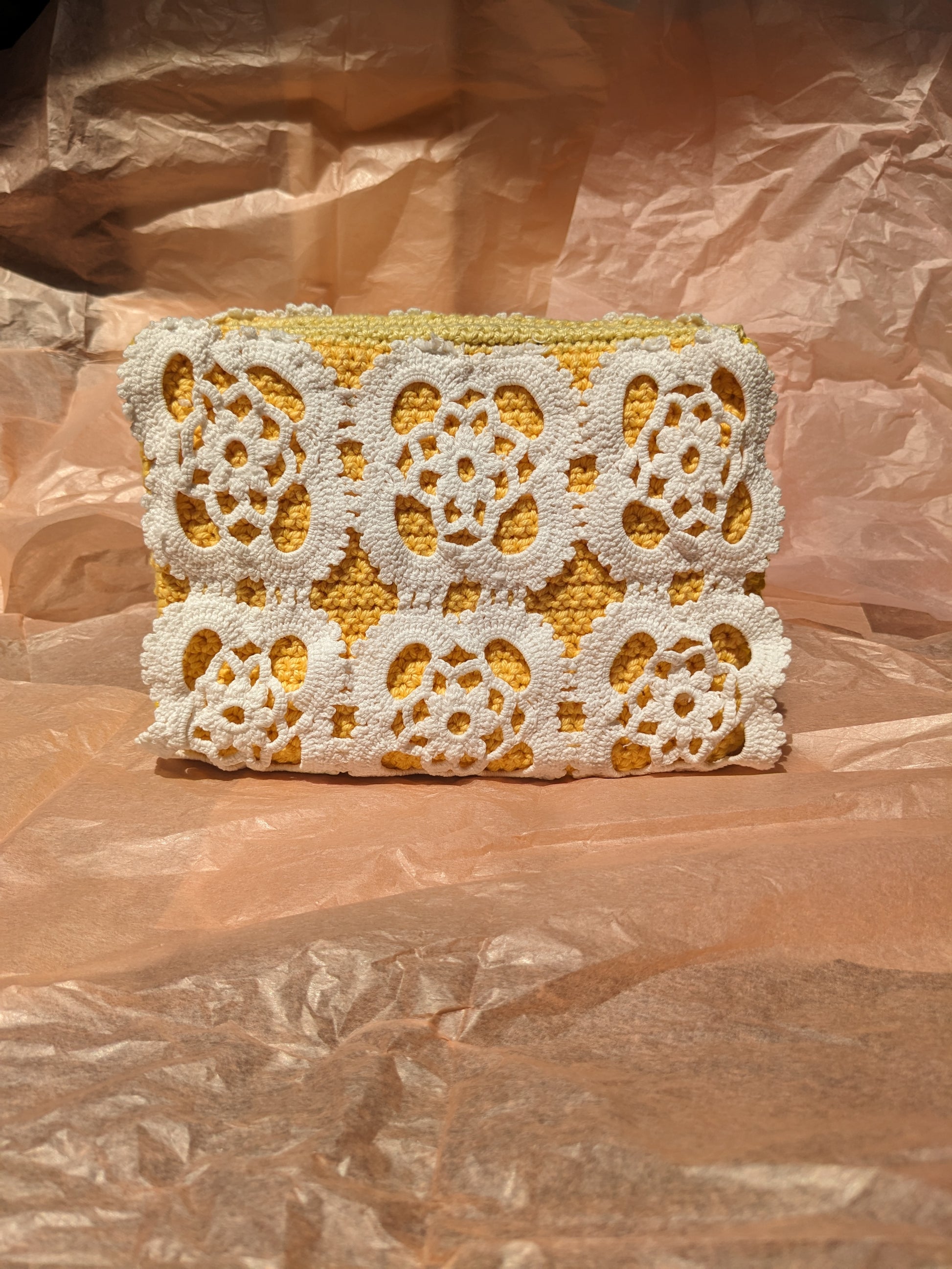 Crocheted upcycled clutch bag with white floral patterns on a pink textured background