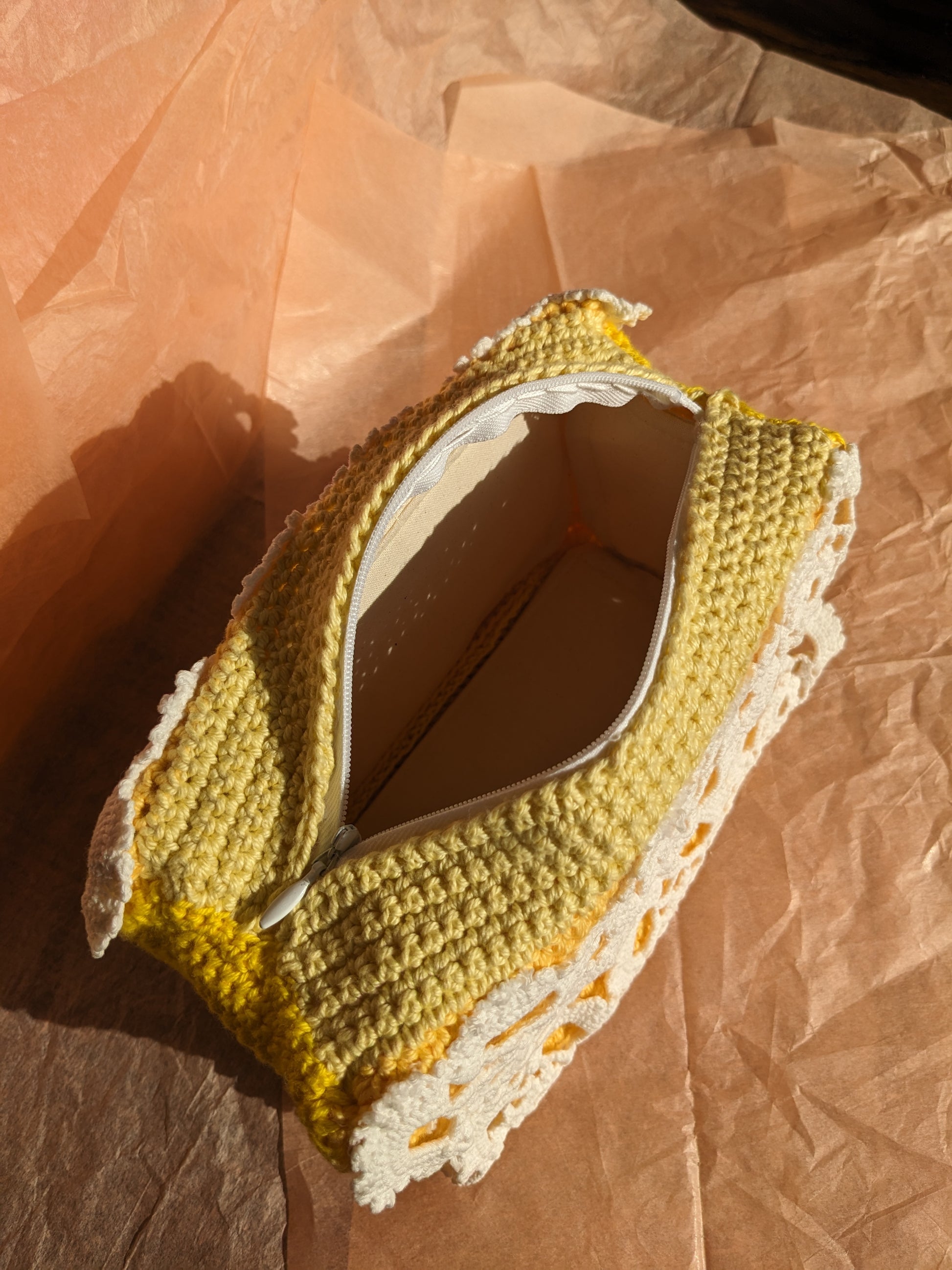 Yellow upcycled crochet vanity bag with white lace trim on pink paper