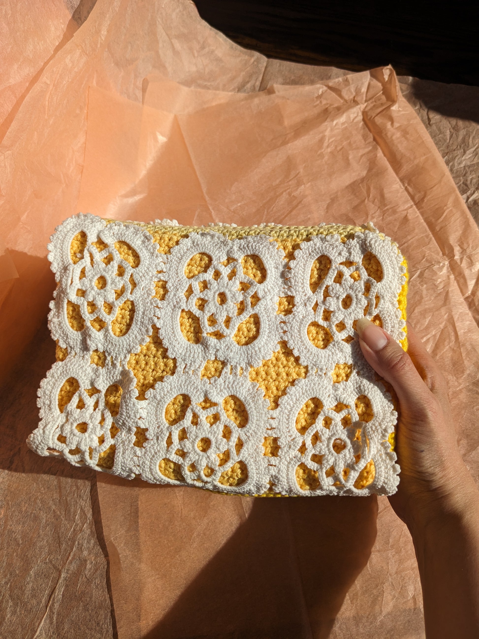 Hand holding a white lace upcycled crochet vanity bag with yellow accents against a pink background