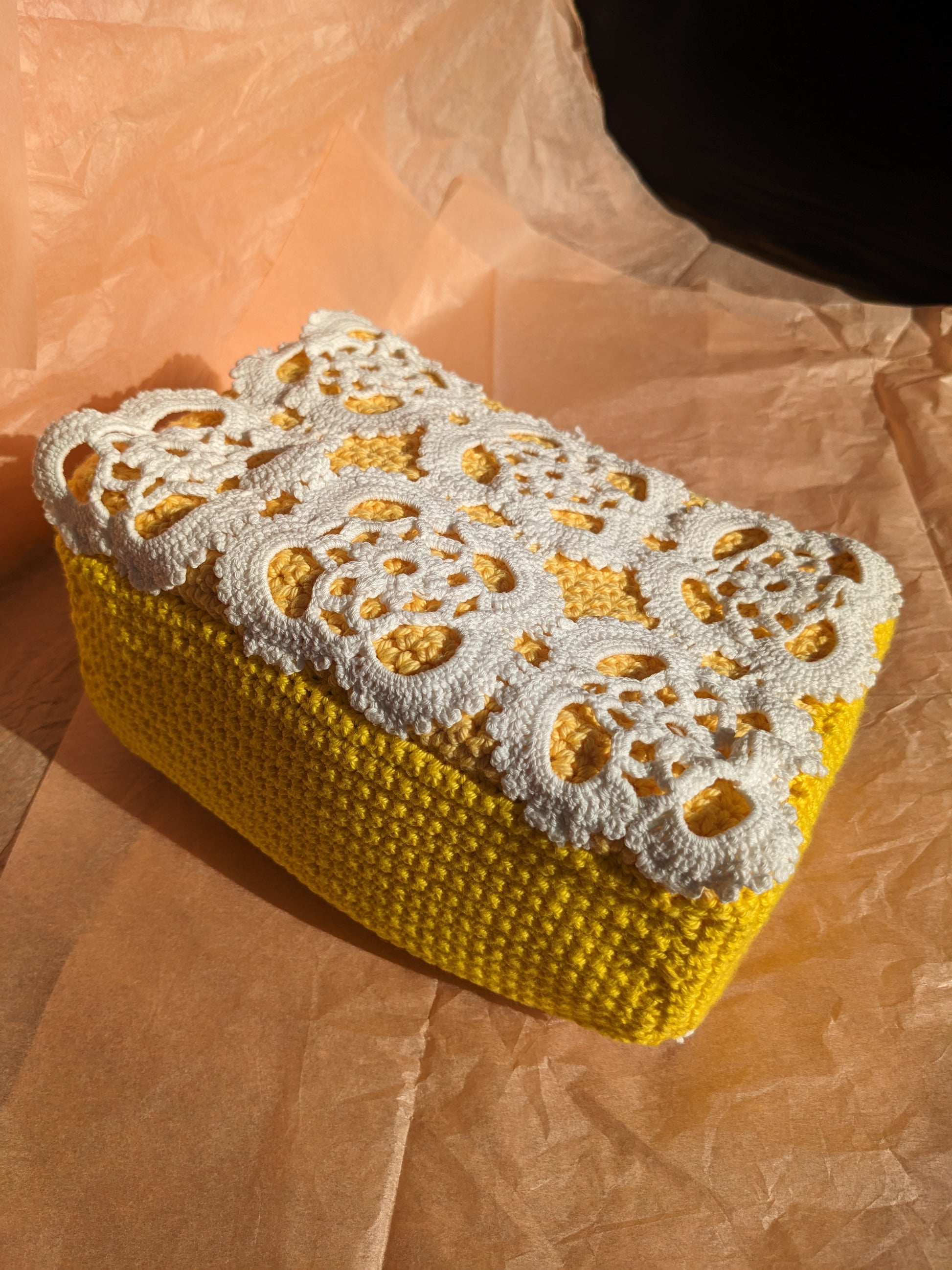 Yellow upcycled crocheted vanity bag with white lace lid on pink paper