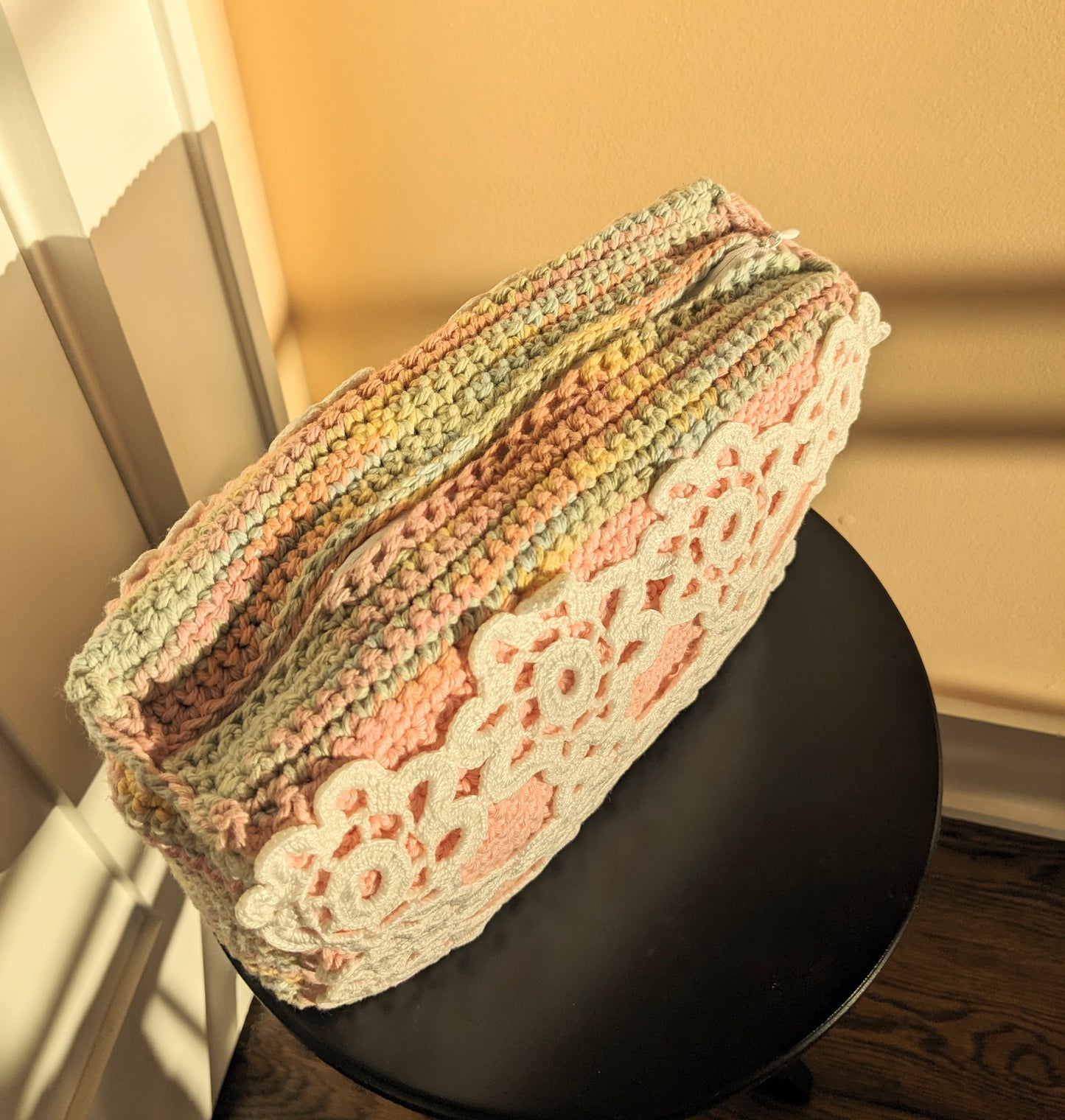Upcycled crochet pink and rainbow clutch on a black stool against a white and salmon background
