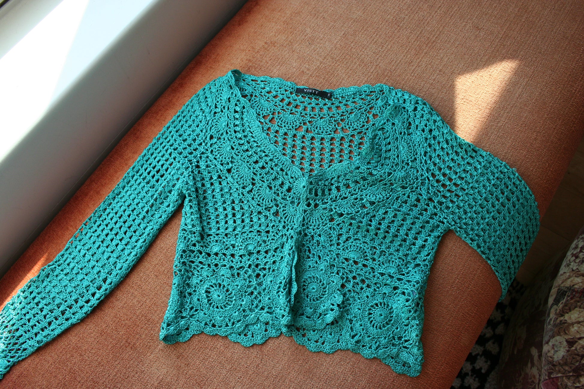 Boho turquoise crochet vest laid flat on the couch