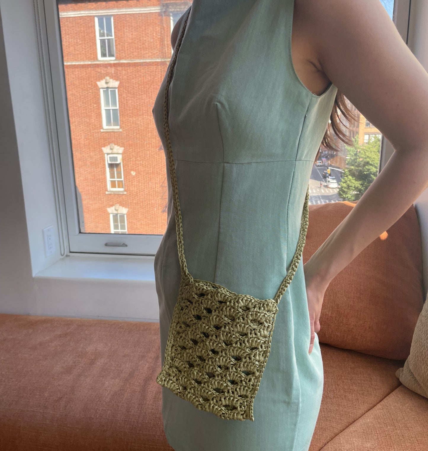 Model wearing the crossbody bag in avocado color, and handmade with raffia.