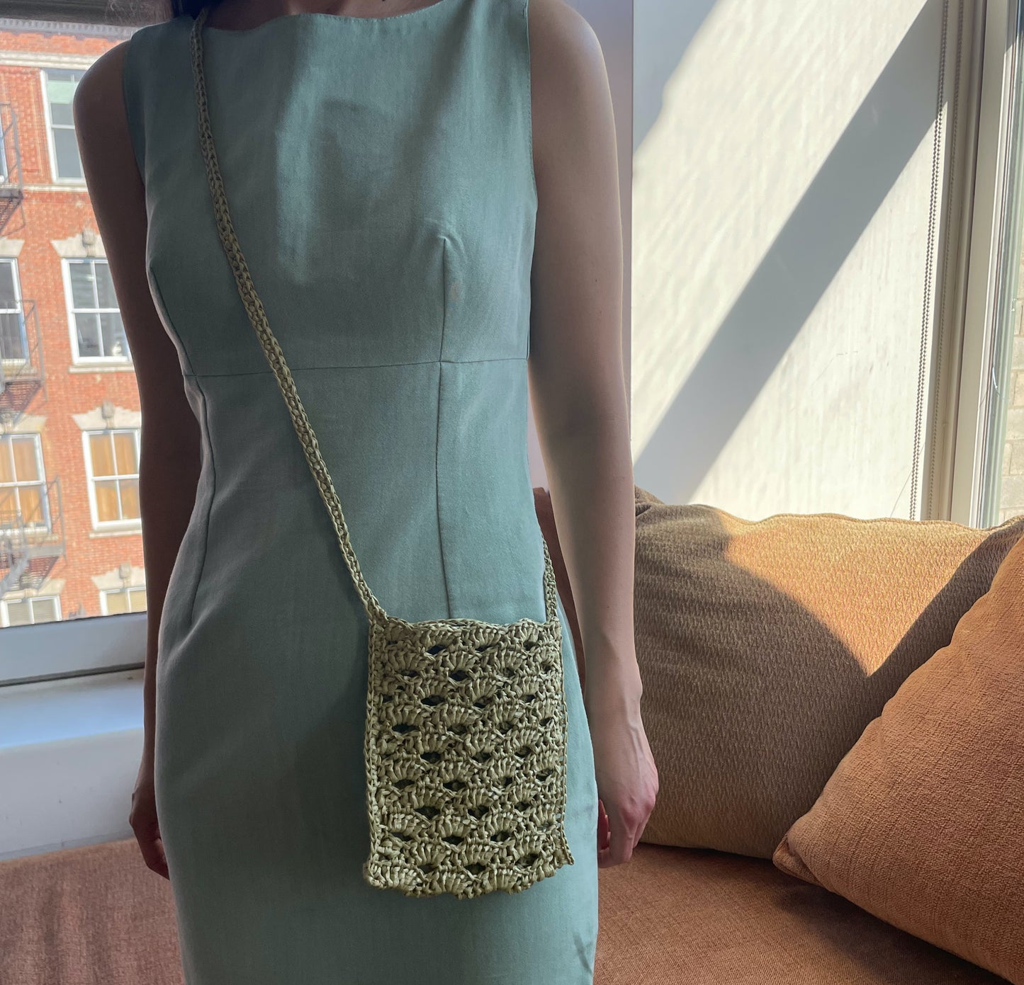 Model wearing the crossbody bag in avocado color, and handmade with raffia.