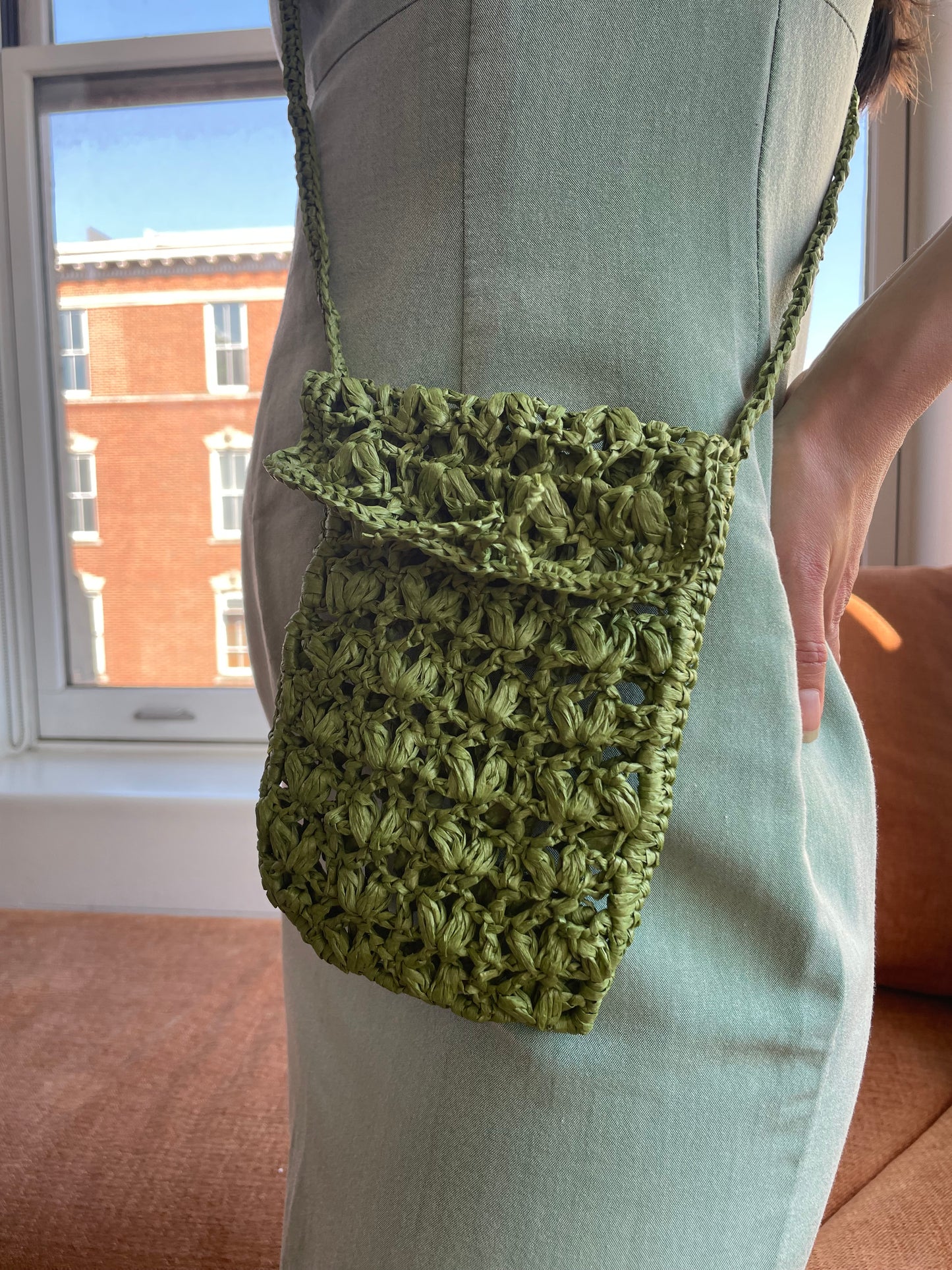 Model wearing the crossbody bag handmade with raffia, in dark green.