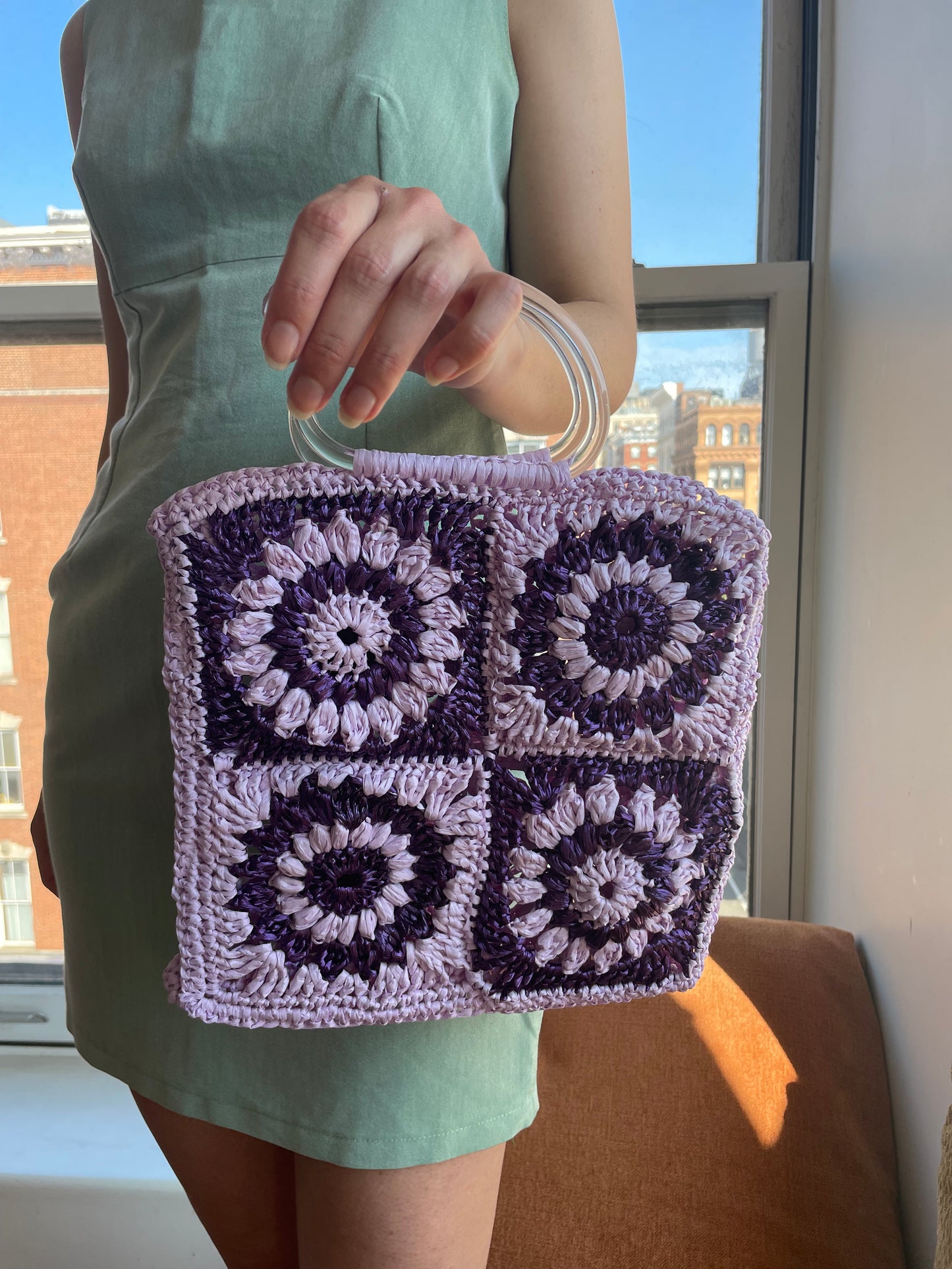 Model holding the granny square raffia crochet bag in lilac