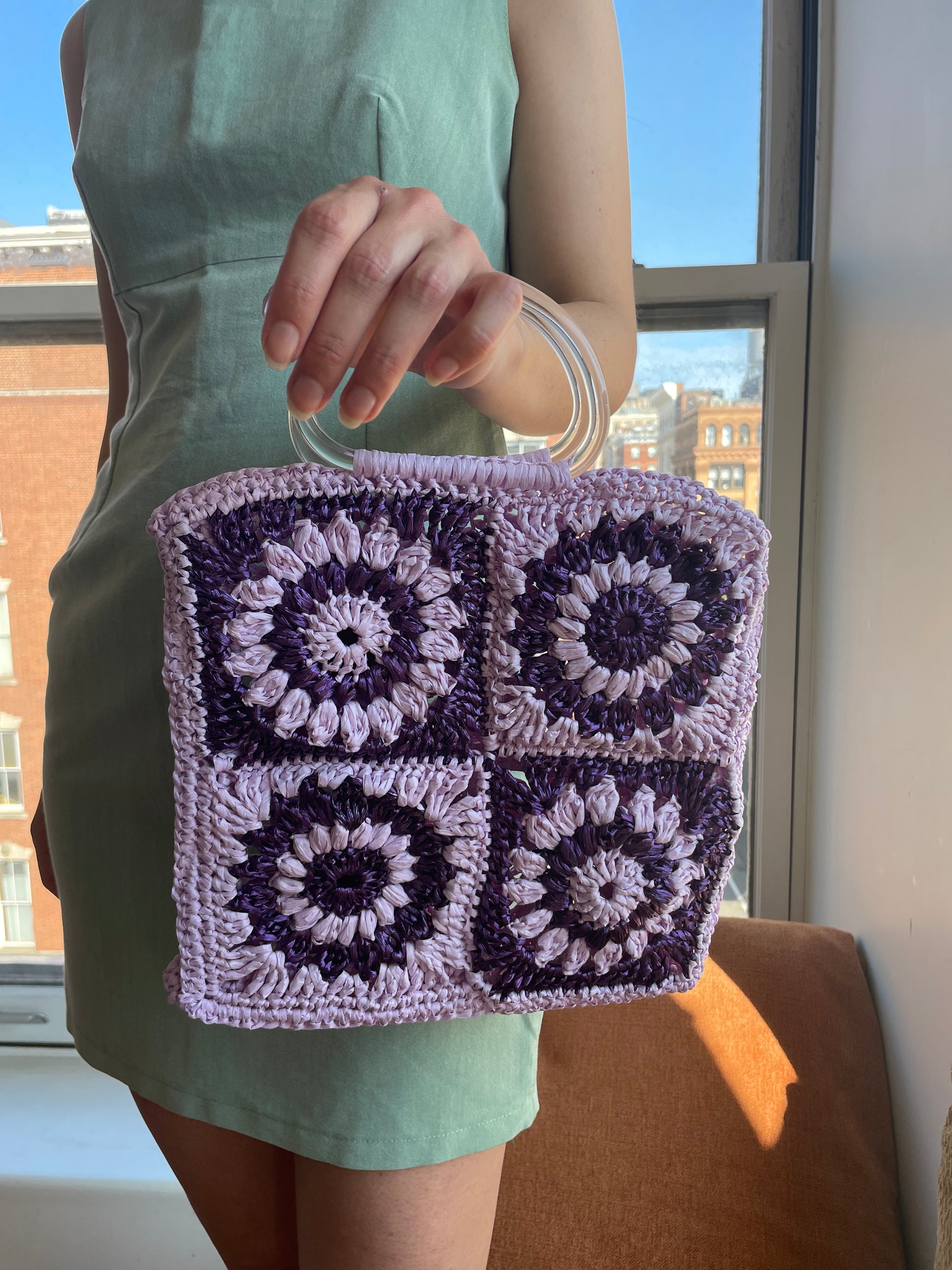 Model holding the granny square raffia crochet bag in lilac