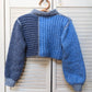 Blue knitted sweater on a wooden hanger against a white wooden background