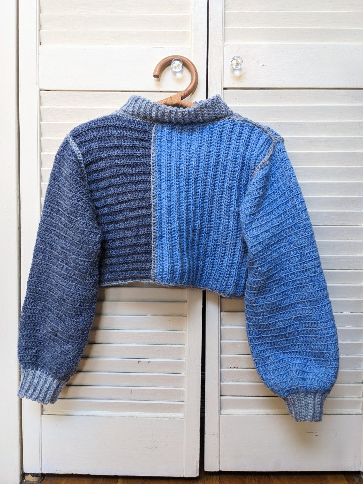 Blue knitted sweater on a wooden hanger against a white wooden background