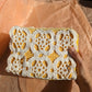 Hand holding a white lace upcycled crochet vanity bag with yellow accents against a pink background