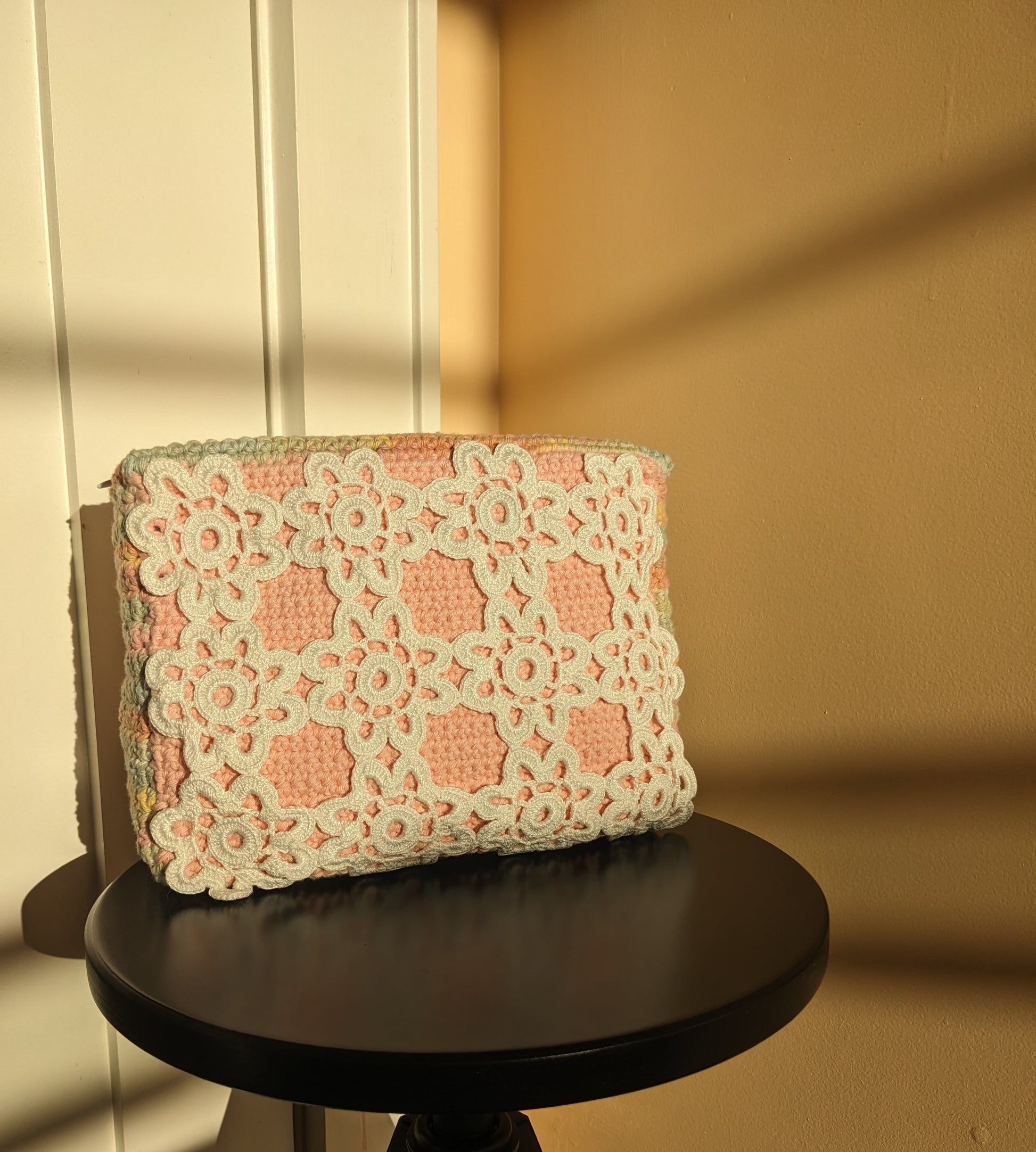 Pink and white lace clutch crochet bag on a black stool against a beige and salmon wall