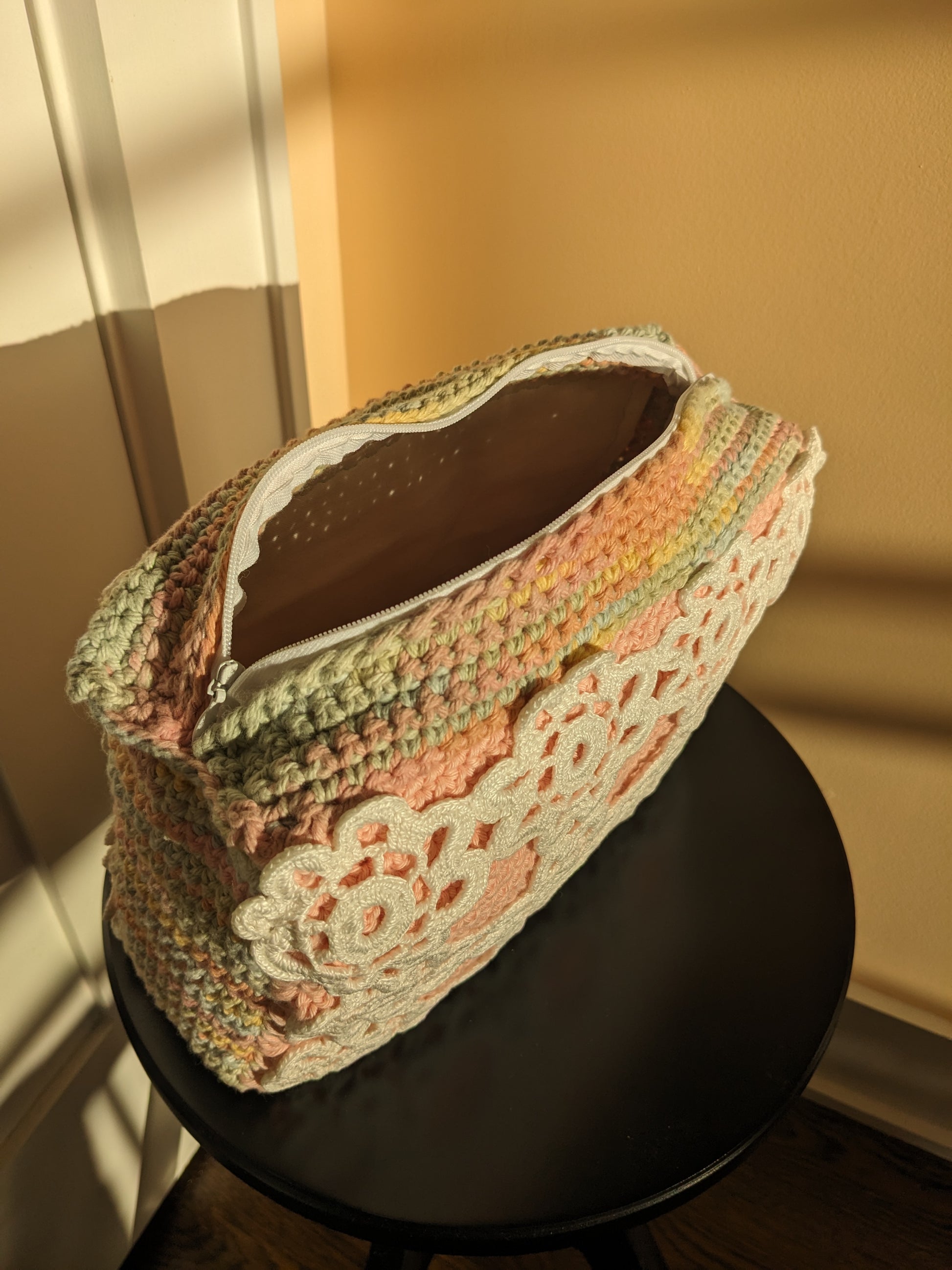 Multicolored crochet ucpcycled bag with lace detail on a black stool against a beige and salmon wall.