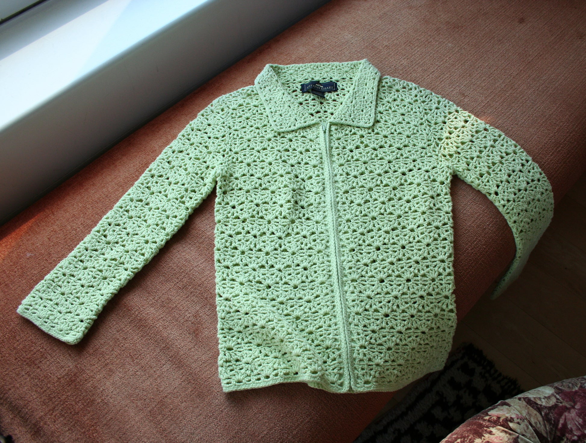 Green flower garden crochet cardigan laid flat on a couch