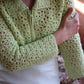 Model wearing the green flower garden crochet cardigan, sitting in an ottoman