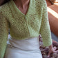 Model wearing the flower garden green crochet cardigan, sitting in an ottoman 