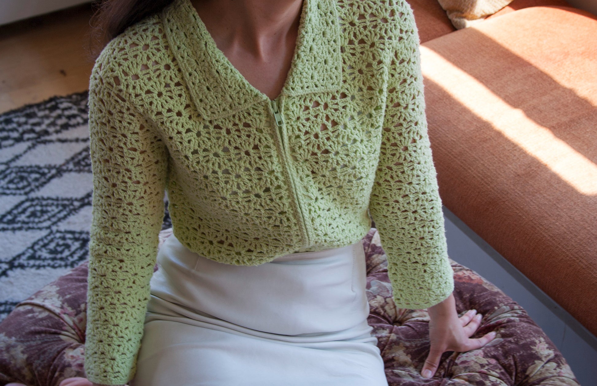 Model wearing the flower garden green crochet cardigan, sitting in an ottoman 