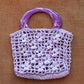 The jazmin raffia bag in lilac laid flat on a couch