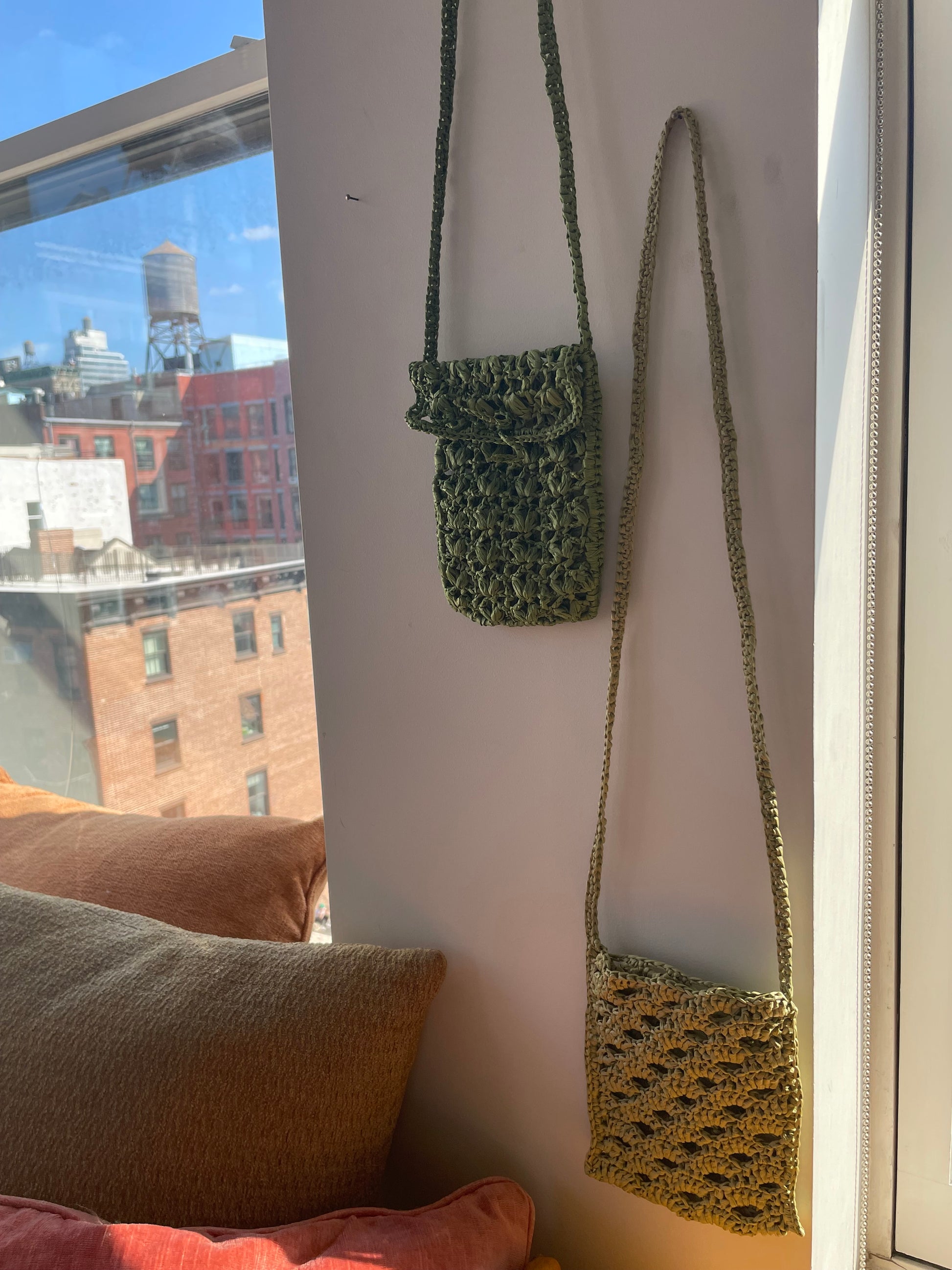 Two crossbody raffia bags in green tones, hung onto the wall 