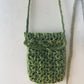 Crossbody raffia bag in dark green hung onto the wall 