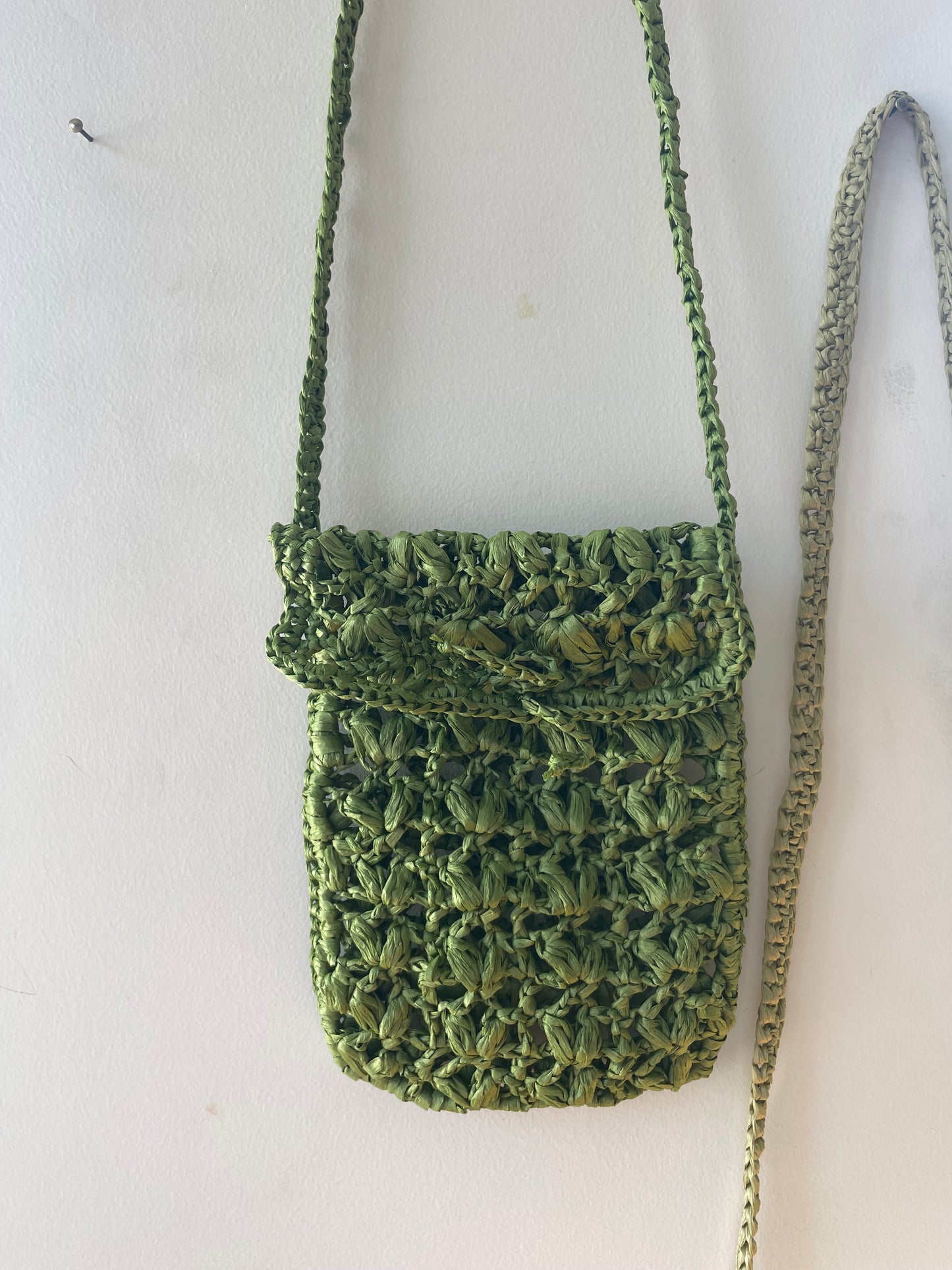 Crossbody raffia bag in dark green hung onto the wall 