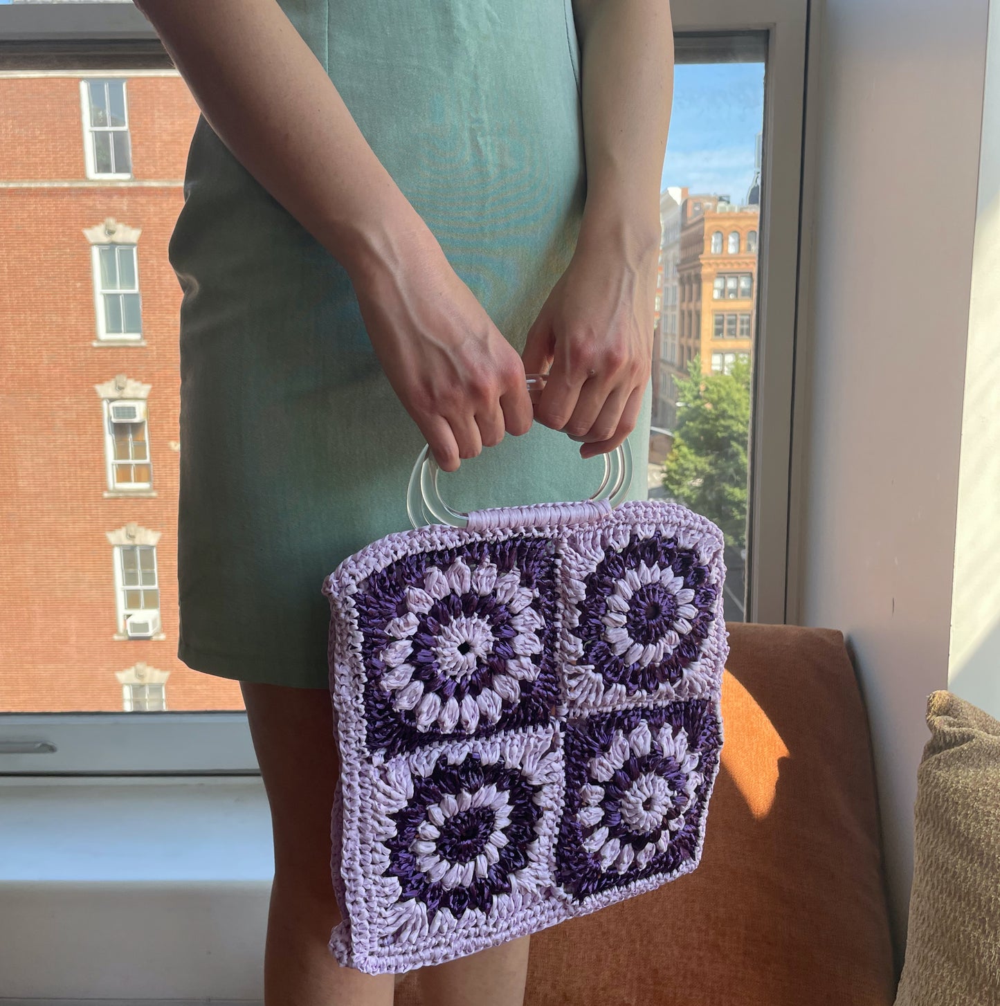 Model wearing the Granny square frame bag made in purple and lilac raffia. 